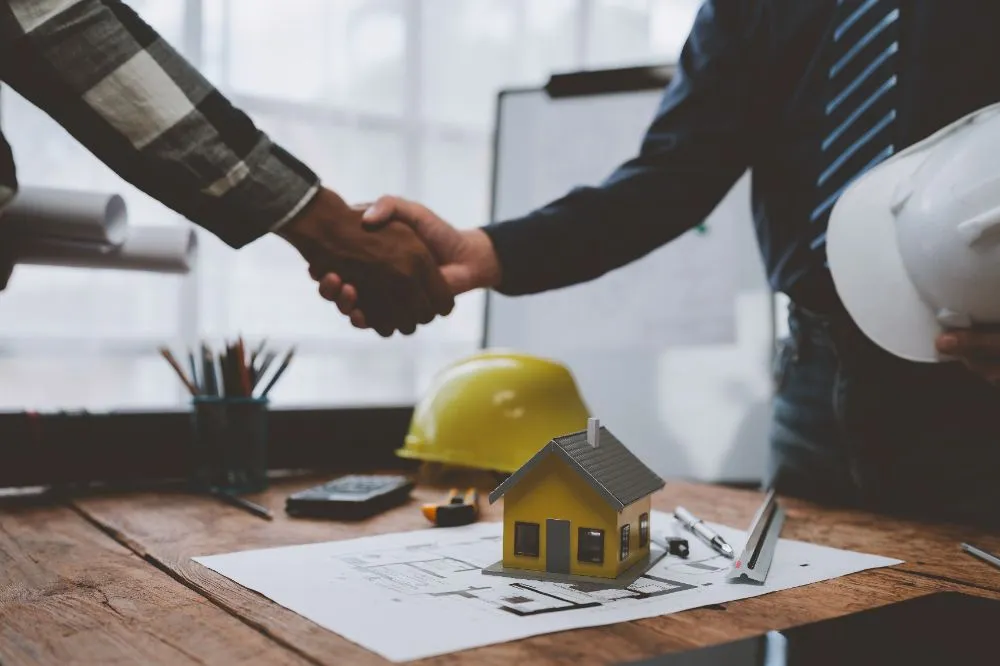 two people shaking hands on top of a house model