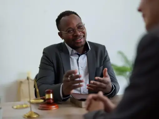 Advocate discussing a case with a client over a desk with the scales of justice and a gavel